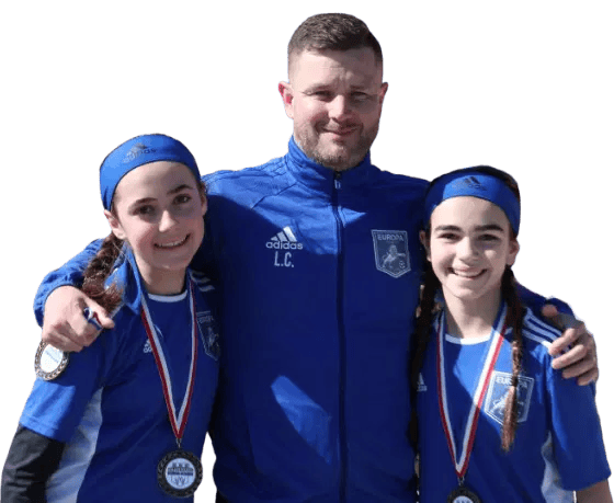 Soccer coach with two young female players in blue jerseys, smiling with medals, team spirit, youth sports, outdoor event.